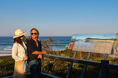 Couple looking at information sign overlooking beach