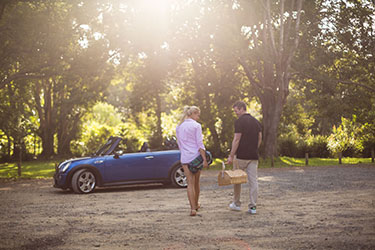 Couple with picnic basket walking towards convertible in hinterland
