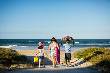 Three kids walking towards beach with buckets and boards