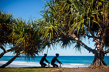 Bike riders under pandanus tree with Shelly Beach in background