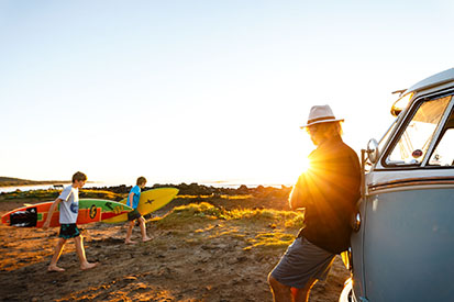 Young surfers running towards beach with dad watching