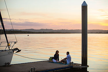 Couple sitting on Lance Ferris Wharf with boat moored