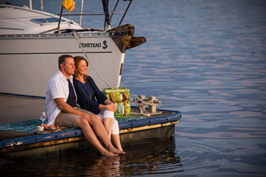 Couple sitting on Lance Ferris Wharf with boat in background