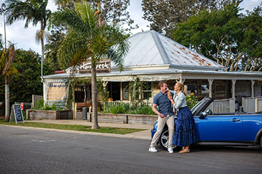 Couple out front of Harvest cafe leaning on convertible