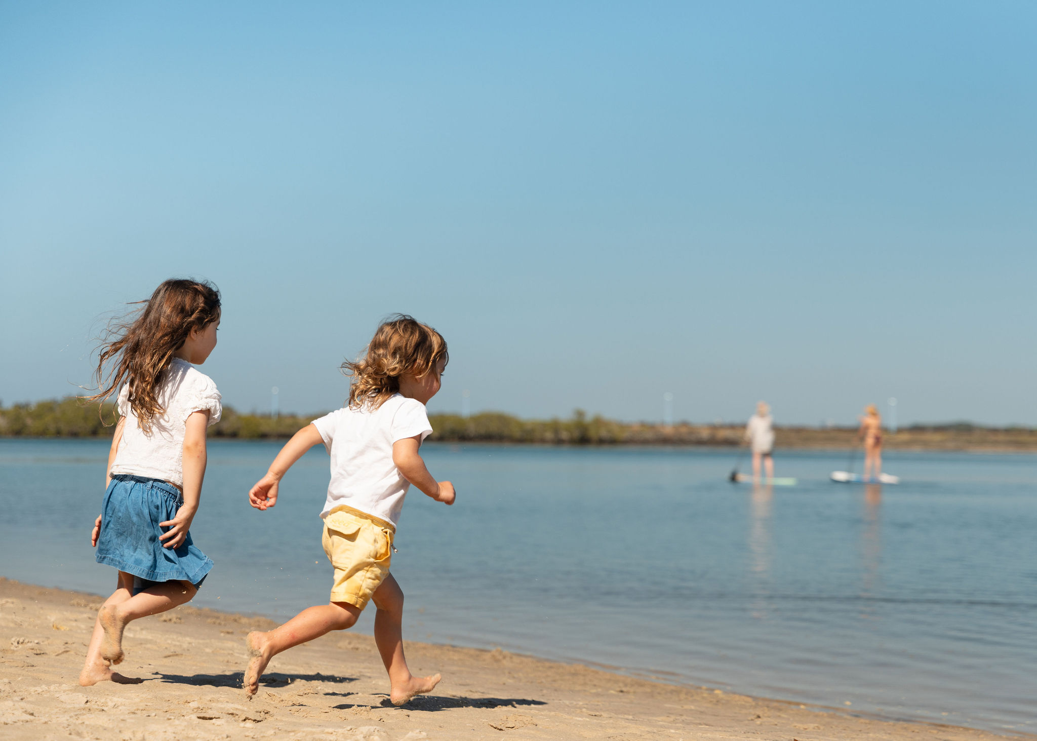 boy and girl running towards water with 2 SUPS in background