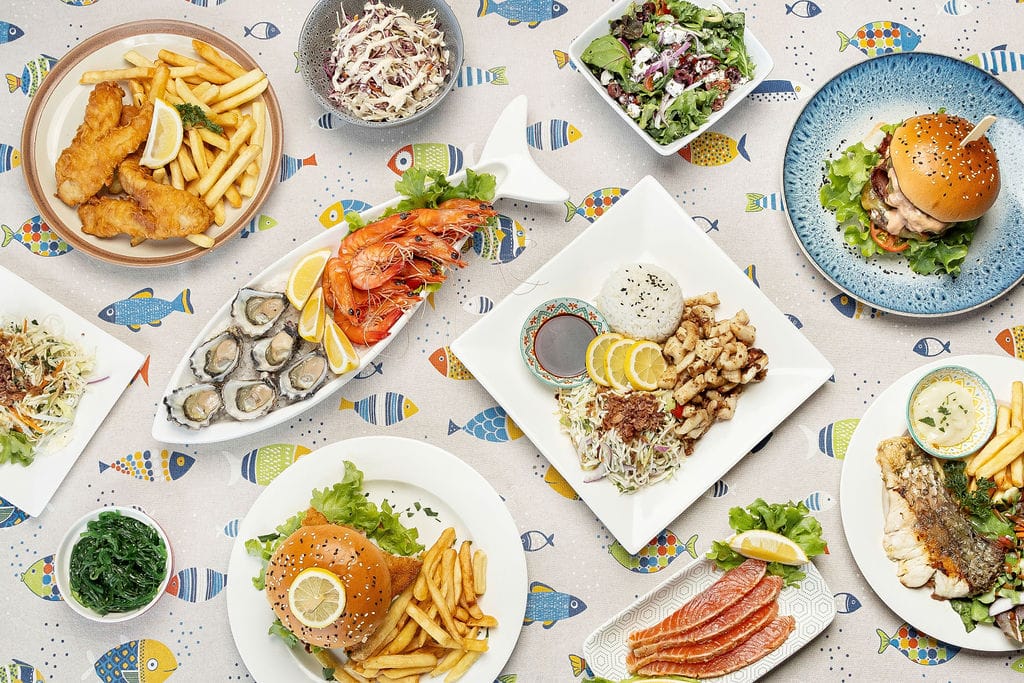 Seafood Dining at Fishy Fishy Lennox Head – Coastal Flavours on a Plate Seafood spread at Fishy Fishy Restaurant Lennox Head featuring oysters, prawns, fish and chips, burgers, and salads on a colourful coastal tablecloth