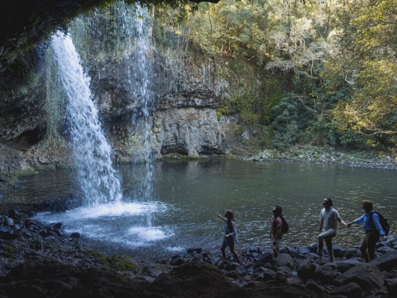 Four hikers explore the rocky path behind the cascading Killen Falls, surrounded by rainforest in the Ballina hinterland, NSW