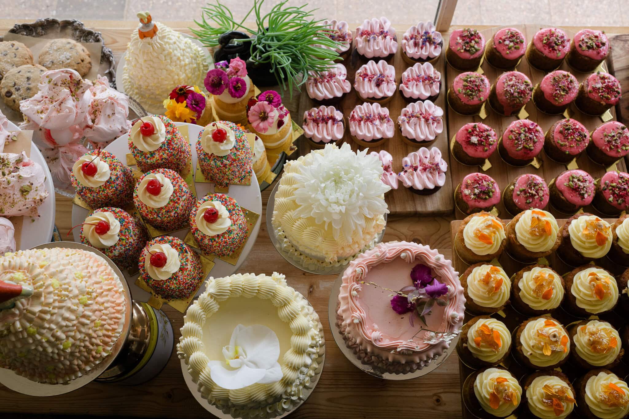 Assorted cakes, cupcakes and desserts on display at HOME Alstonville, including floral buttercream cakes and pink iced treats.