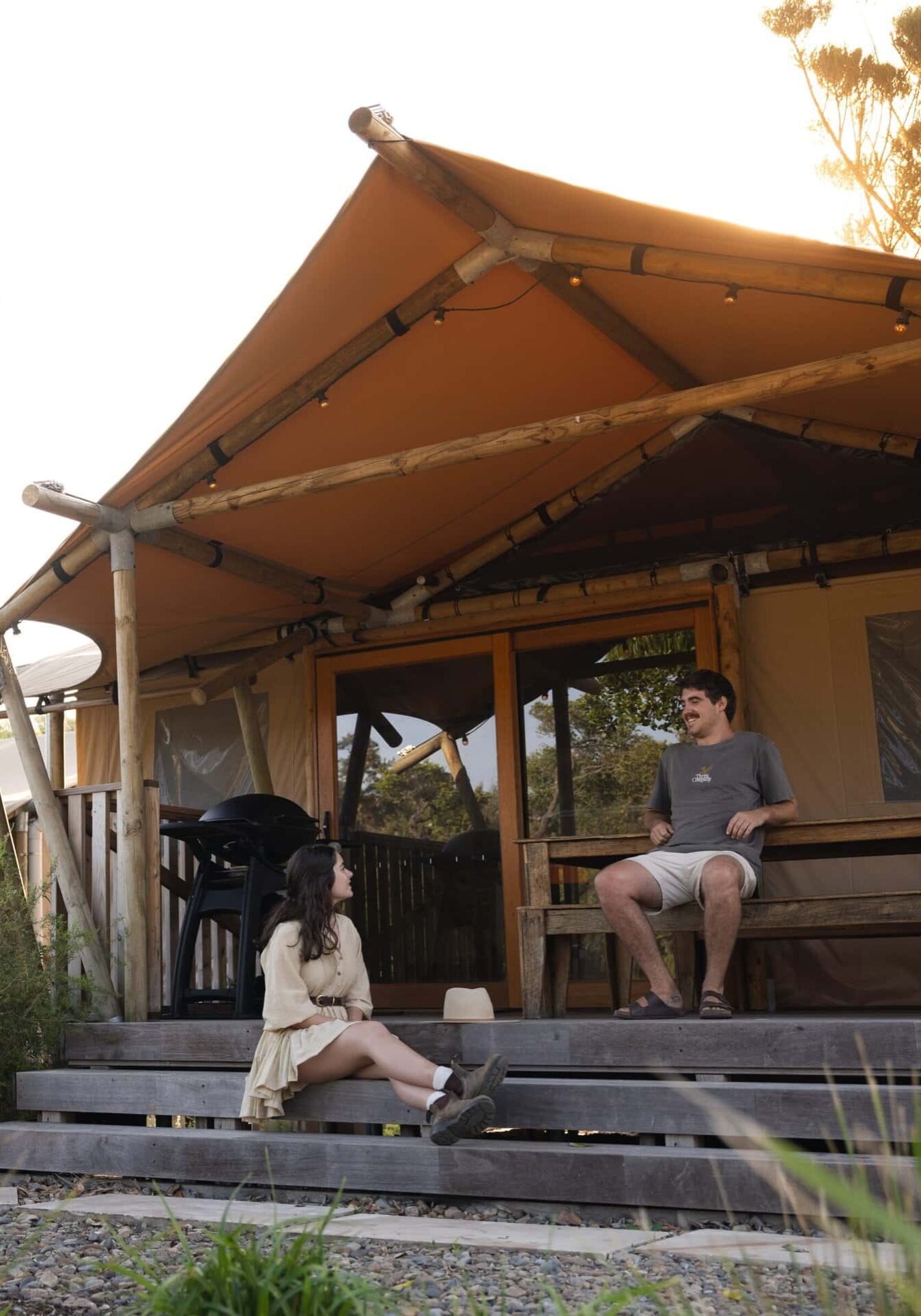Glamping Tent Stay – Ballina Beach Nature Resort, NSW Couple relaxing outside a luxury glamping tent at Ballina Beach Nature Resort in South Ballina, surrounded by native bushland and coastal greenery.