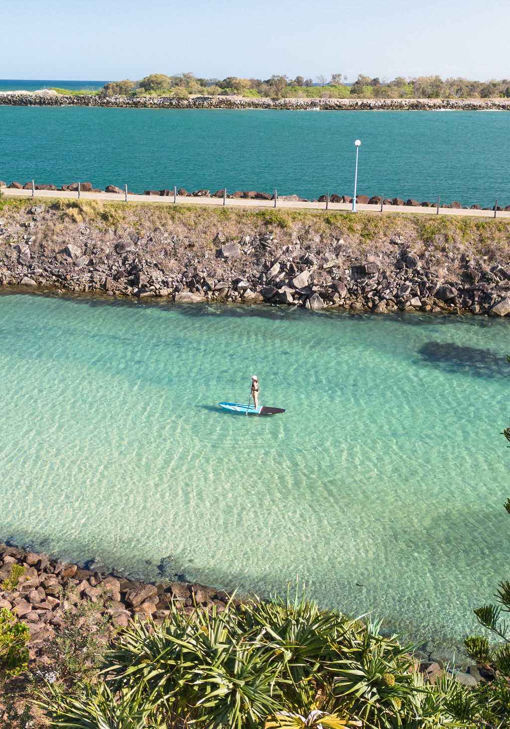 Stand-up paddleboarder gliding across the clear waters of Shaws Bay in Ballina.