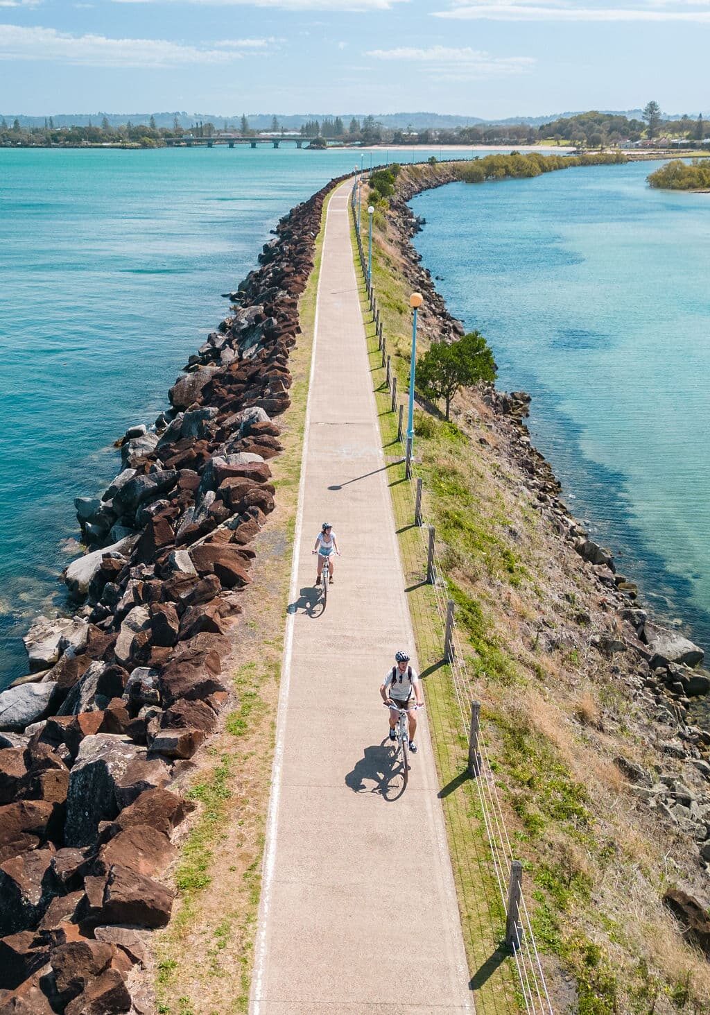 Cyclists riding along the North Wall pathway in Ballina, with ocean on one side and the Richmond River on the other.