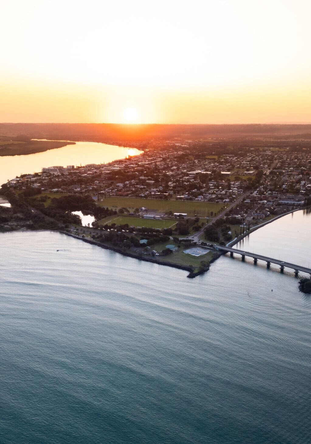 Sunset Over Ballina, NSW – Coastal Charm from Above Aerial view of Ballina, NSW at sunset showing the Richmond River, coastline, and townscape bathed in golden light.