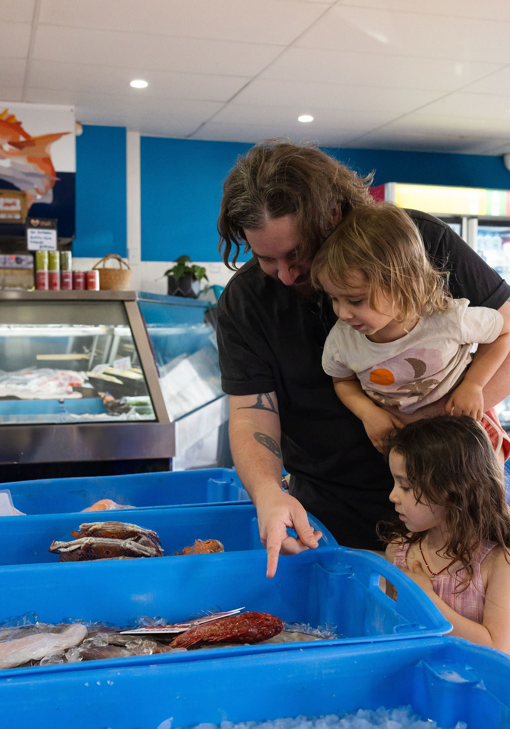 An adult and two young children looking at fresh seafood in blue tubs inside a local Ballina fish shop