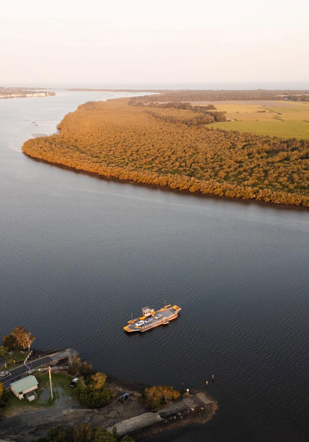 Burns Point Ferry Crossing the Richmond River – South Ballina, NSW Aerial view of the Burns Point Ferry transporting vehicles across the Richmond River between Ballina and South Ballina, with mangroves and farmland in the background.